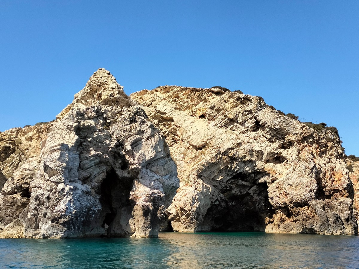 Rocky coastal arch formation with clear blue sky and water.