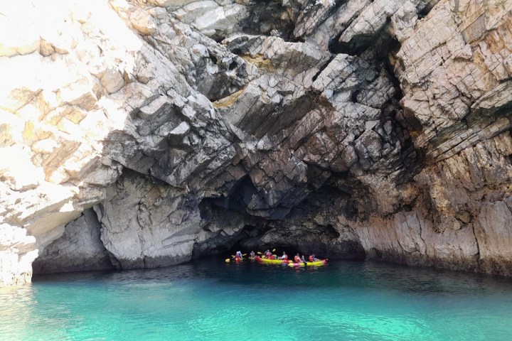 Kayakers entering a rocky sea cave over turquoise water.