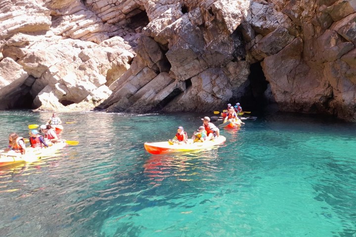 Kayakers paddle near rocky cliffs in clear turquoise water.