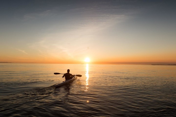 Person kayaking on calm water at sunset.