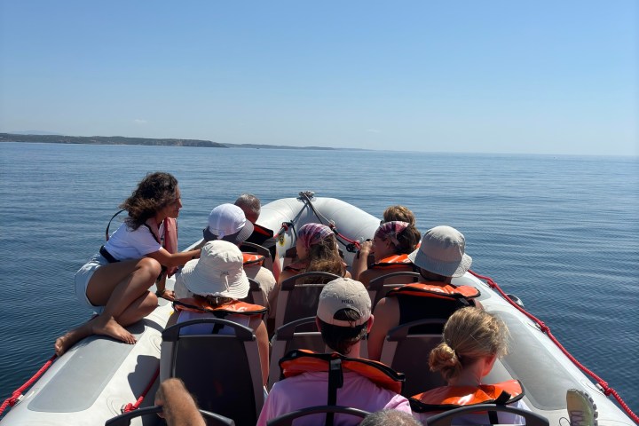 Group on inflatable boat, wearing life jackets, under clear blue sky.