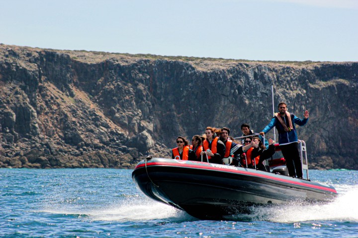 Group on a motorboat with life jackets cruising near rocky cliffs.