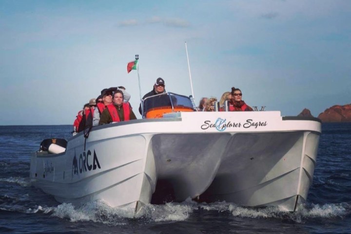 Tourists on a white boat named ORCA, cruising on open water under a clear sky.