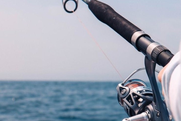 Fishing rod held over ocean with clear sky.