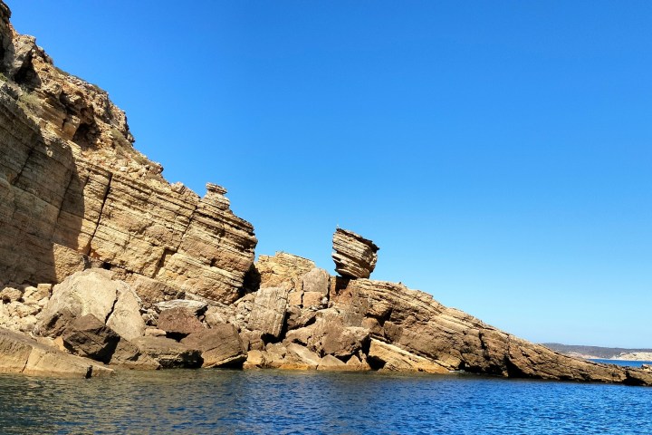 Rocky cliff by a calm blue sea under a clear sky.