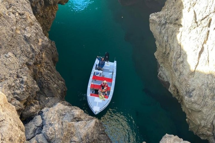 Boat with people inside a rocky cave, surrounded by turquoise water.