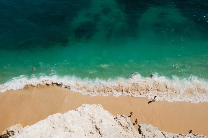 Aerial view of sandy beach with turquoise waves and people swimming.