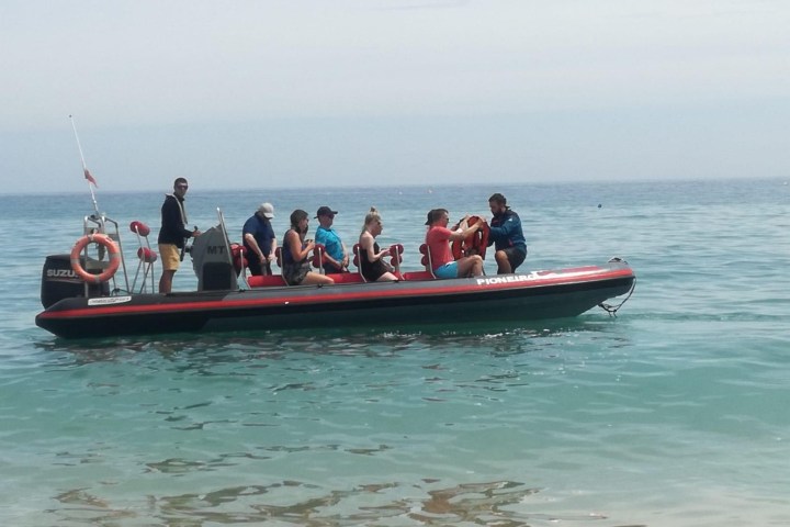 People sitting on a red inflatable boat on calm sea waters.