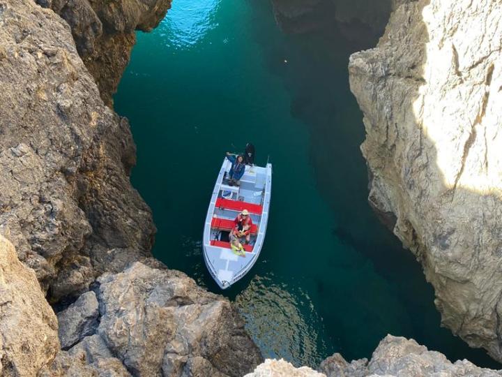 Boat with people in clear turquoise water surrounded by tall, rocky cliffs.