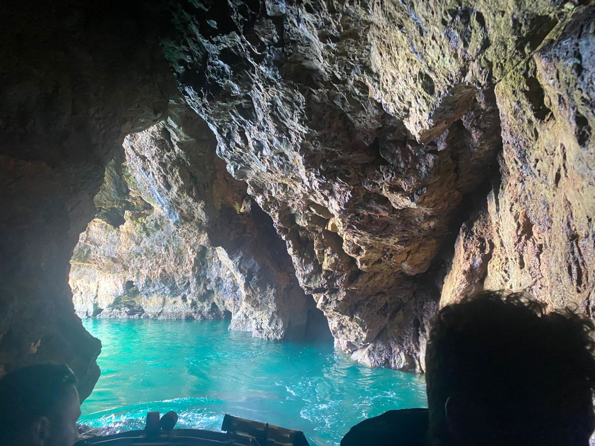 Sunlit cave with turquoise water viewed from inside a boat.